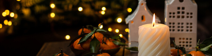 Banner. Burning scented candle with the smell of citrus, gingerbread cookies, cinnamon, anise. Comfort at home, creating cozy festive holiday atmosphere at home. Atmospheric fairy lights. Aromatherapy