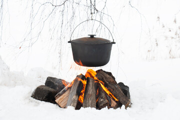Above the fire hangs a pot in which food and tea are prepared. Winter camping, outdoor cooking