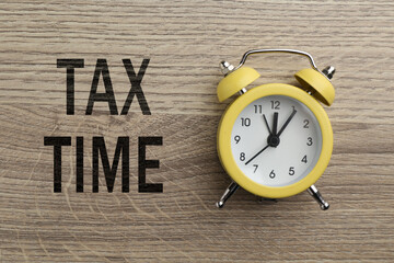 Tax time. Alarm clock on wooden background, top view