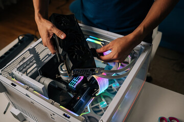 Skilled computer professional inserting high-performance graphics card into custom gaming pc, illuminating interior with vibrant RGB lighting for enhanced visual experience.