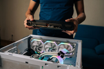 Computer technician installing powerful new graphic card into custom-built gaming pc, featuring vibrant RGB lighting and advanced water cooling system for optimal performance.