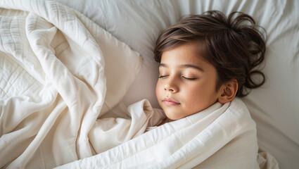 Peaceful young boy sleeping soundly wrapped in a soft, cozy blanket on a white bed
