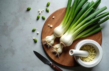 Fresh wild garlic bulbs, green stalks arranged on wooden board near mortar filled with chopped garlic. Knife lies beside cutting surface, suggesting preparation for cooking. Scene evokes natural,