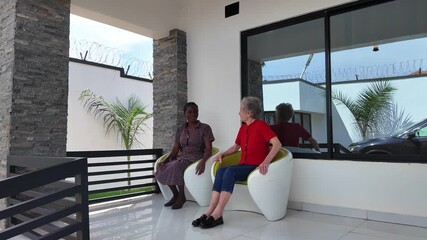 Lilongwe Malawi Africa, 01.12.2025. Video. African female  carer sitting on a patio working with an elderly Dementia sufferer  on holiday in Malawi Africa.