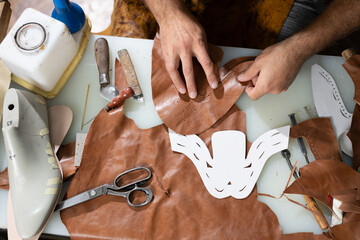 Leather workshop scene of hands crafting a decorative mask with tools and templates