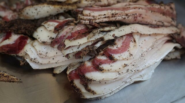 Close-up of seasoned sliced guanciale pork cheek with black pepper, used as a traditional ingredient for Roman carbonara pasta. Authentic Italian cuisine, raw meat texture and food preparation concept