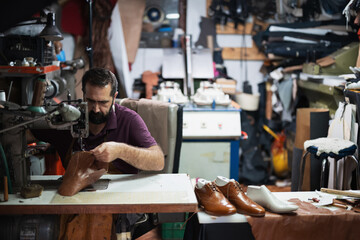 Shoemaker at work in busy workshop sewing leather shoes by hand