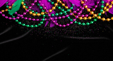 Mardi Gras beads and feathers in purple, green, and gold cascade over black fabric with glitter