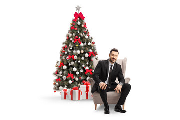 Professional man in a black suit sitting in an armchair by the christmas tree