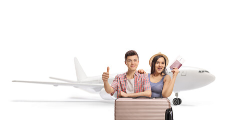 Young male and female passengers with a passport and a suitcase posing in front of a plane