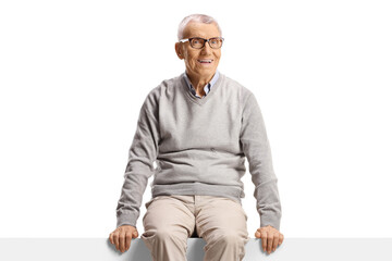 Cheerful elderly man sitting on a blank panel and smiling