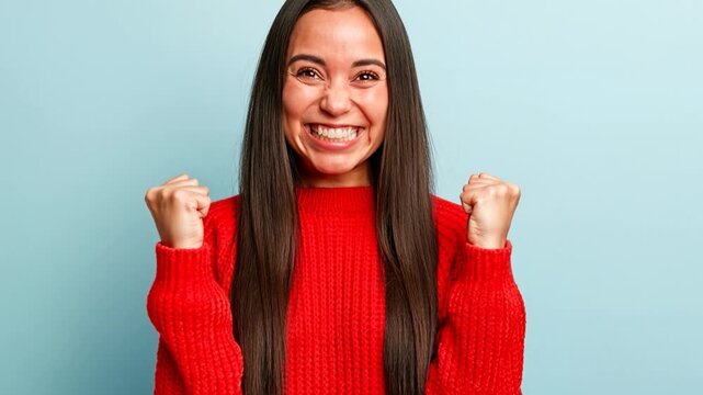 Successful female student happy to get scholarship, clenches fists, accomplishes goal, exclaims finally victory, stands amused over blue background. 
