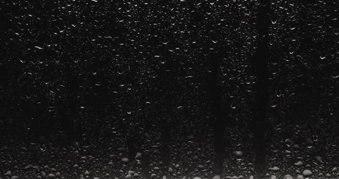 Close-up drops of water sliding down on the glass surface over black background.  