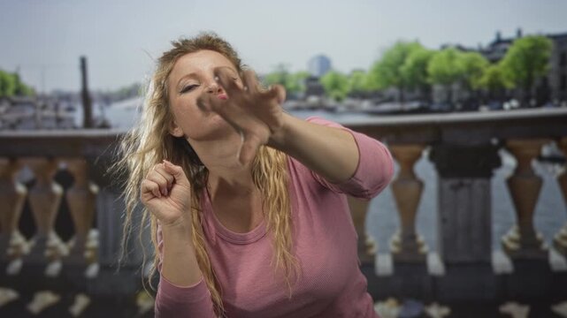 Woman reaches right hand forward while puckering lips and making a claw gesture near face on amsterdam street canal bridge; playful teasing.