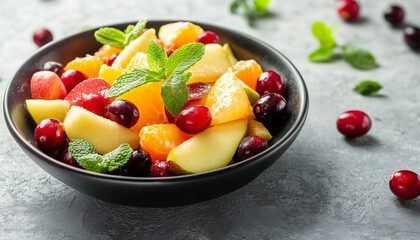 Fresh fruit salad in a bowl with cherries, orange, pear, and mint leaves. Colorful mix of fruits on gray background. Healthy dessert or