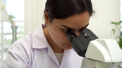 Focused young Middle Eastern female scientist looking through microscope in laboratory. Concentrated woman researcher or student analyzing biological sample for medical experiment concept.