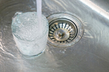 Glass Filling With Fresh Water.Clear glass being filled with fresh tap water in a stainless steel sink, symbolizing cleanliness, hydration, domestic routine, and safe drinking water concept.