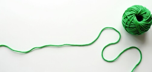 Green thread unspools from ball on white backdrop, creating flowing wavy line. Ample clean copy space for text or graphics. Simple abstract backdrop.