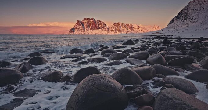 Winter landscape with snow covered mountains peaks, rocky coastline and scenic sunset over Uttakleiv Beach, Lofoten Islands, Norway