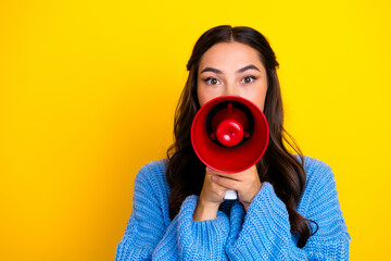 Fototapeta premium Young woman with red megaphone speaks to audience in a bright yellow studio wearing a blue sweater