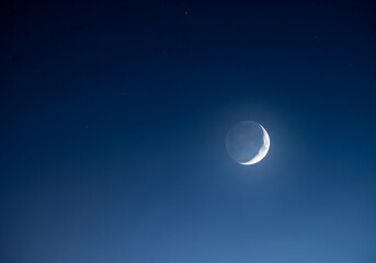 Dramatic crescent moon illuminating a deep twilight sky, casting a serene glow amidst the fading light, creating a cinematic celestial scene