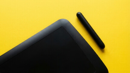 Black graphic tablet and stylus on a bright yellow background, minimalist composition