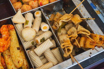 A variety of colorful Korean street food snacks, including fish cake, fish balls, surimi, and chikuwa, are neatly organized in metal compartments at a food stall.