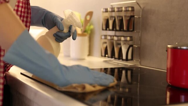 Woman spraying cleaning product while wiping dust from cooktop in kitchen, closeup. Camera moving in