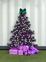 Decorated Christmas tree with purple ornaments and pile of presents beneath in room interior