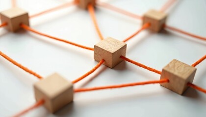 Wooden cubes linked by orange cords form abstract network pattern. Symbolizes connection, teamwork, communication, and structure. Simple design on white background.