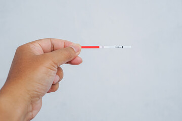 A hand holds a pregnancy test strip showing two red lines, indicating a positive result. Set against a plain white background, symbolizing a life-changing moment