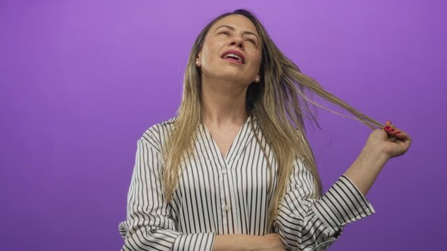 Woman touching blonde hair with playful gesture and tilting head in purple studio; contemplation wonder.