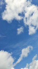 Vertical view of bright blue sky with fluffy white cumulus clouds and wispy natural atmospheric textures.