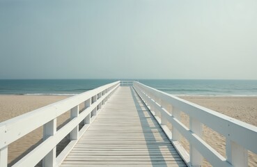 White wooden pier stretches over sandy beach towards calm blue ocean under clear sky. Serene seascape invites peaceful walk along coast. This pathway offers access to seaside.