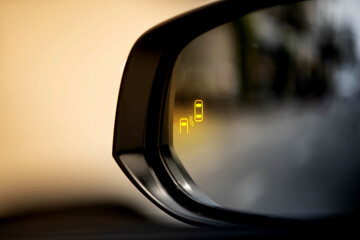 Blind spot monitor (BSM) warning light on car side mirror. Advanced driver assistance system for safety and collision avoidance.
