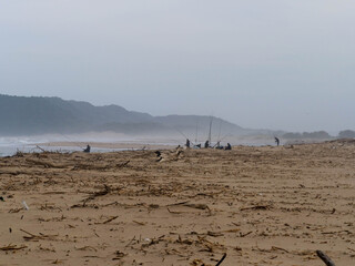 A group of fishermen surfcasting from the beach with with beach sand in the foreground.  Location: St Lucia, KwaZulu Natal