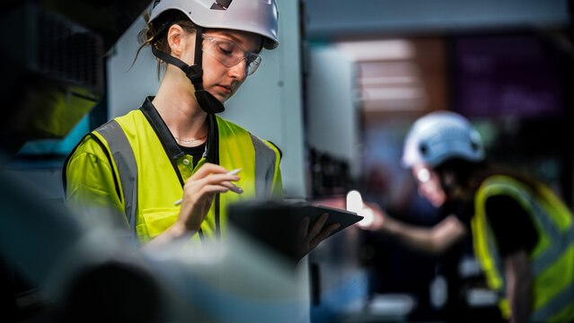 A female robotics engineer in an R and D lab uses a tablet to program an artificial intelligence cobot. She is inspecting the robotic system hardware and software diagnostics. - Powered by Adobe