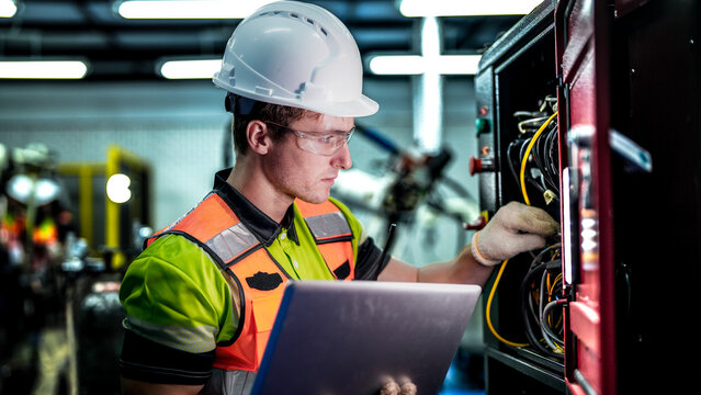 An engineer represents the future of work, using a laptop to manage AI and robotics. This high-tech automation optimizes the manufacturing supply chain.