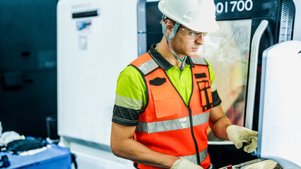 A focused Caucasian male engineer in a hard hat and safety vest operates a high-tech industrial machine. He is a specialist in a futuristic smart factory.