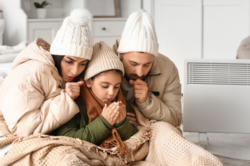 Frozen family with plaid and lack of heating warming near electric convector heater in bedroom