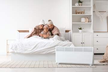 Frozen family with lack of heating and electric convector heater hugging in bedroom