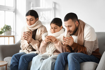 Frozen family with lack of heating drinking hot tea on sofa at home