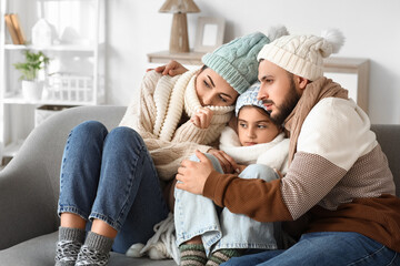 Frozen family in warm clothes with lack of heating hugging on sofa at home