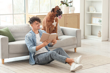 Handsome young man with Boxer dog on sofa reading book at home