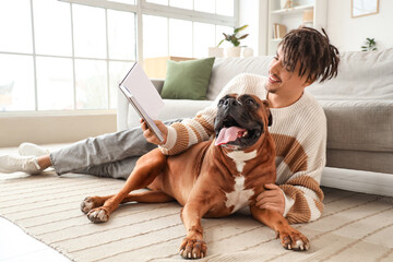Young man with Boxer dog reading book on carpet at home
