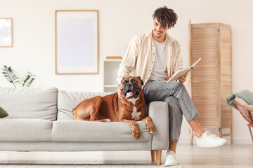 Young man with Boxer dog reading book on sofa at home