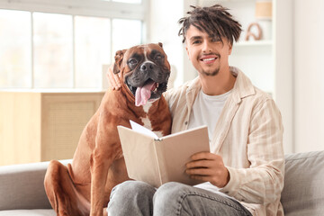 Young man with Boxer dog reading book on sofa at home