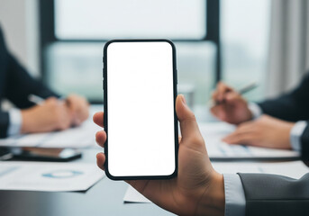 Hand holding a smartphone with a blank white screen in a business meeting environment