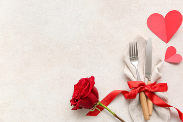 Table setting for Valentine's Day with cutlery, ribbon, rose flower and paper hearts on light...