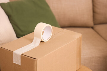 Cardboard box with adhesive tape in room on moving day, closeup